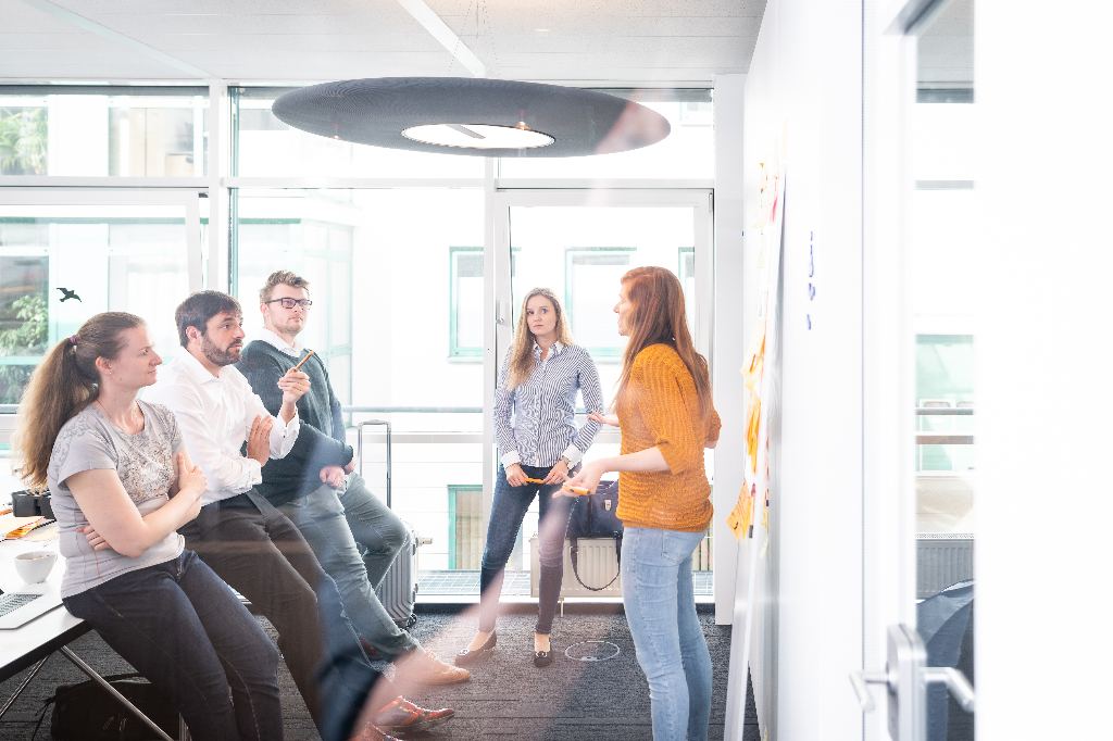 Four participants in the Advanced Certified Scrum Master (A-CSM) training are standing in front of a flipchart and one person is explaining something.