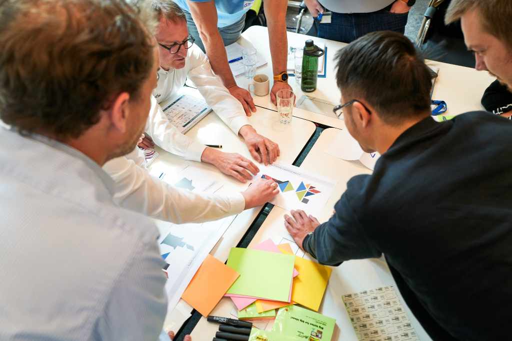 A group of Implementing SAFe Training participants solves a task together. Post Its and the workbook are on the table.