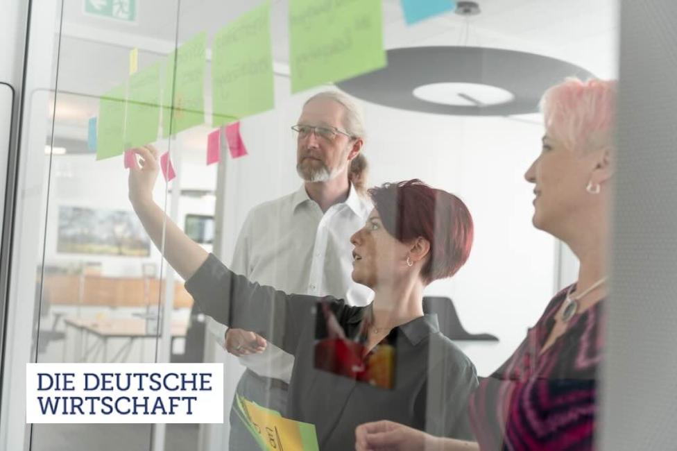 3 Personen arbeiten mit Postits an einer Glaswand