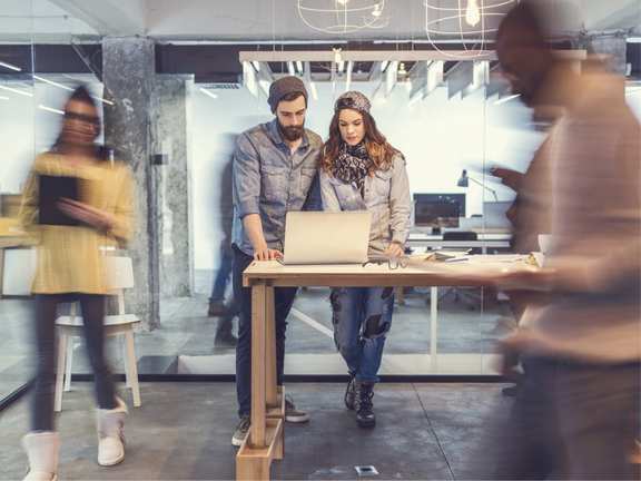 Zwei Menschen stehen an einem Tisch im Büro vor einem Laptop