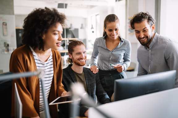 Four young developers, two women and two men, developing an app together as an agile team and just looking at a monitor together