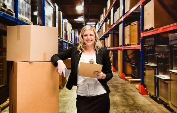 A woman stands in a high rack warehouse and looks directly at the viewer
