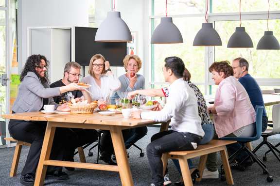 eight employees have breakfast together at a long wooden table