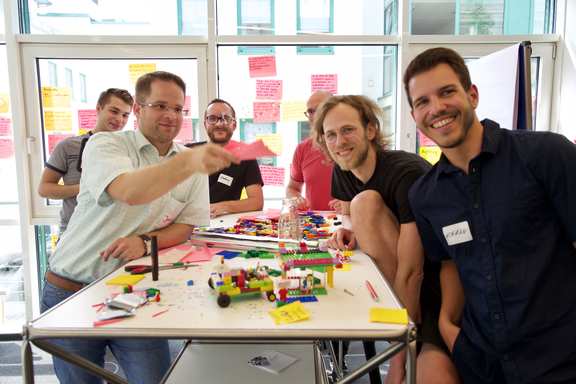 Ein Scrum Team am Tisch, mit eine Lego Gebäude, fertig zum Review