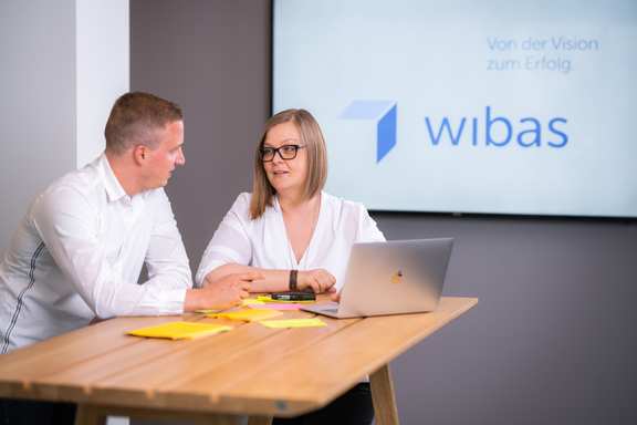 Zwei Personen unterhalten sich an einem Tisch und einem Laptop