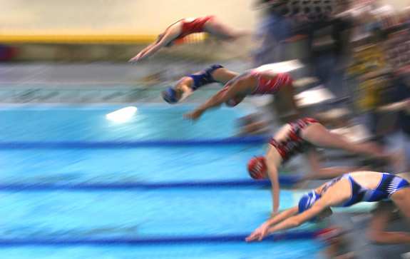 A team of swimmers just jumping into the water. Image has motion blur.
