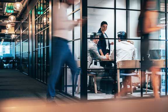 A team in an office, people pass in front of it, with motion blur