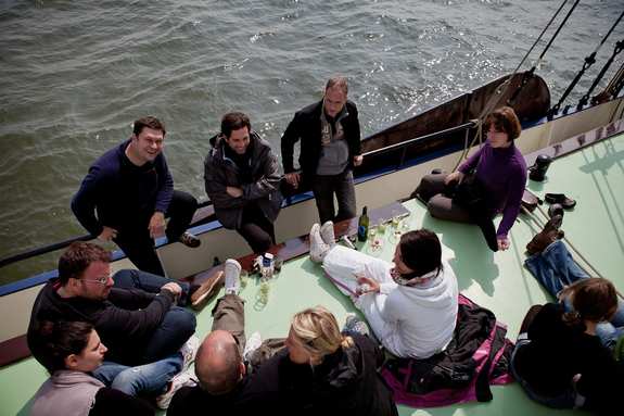 eine Gruppe von Männern und Frauen sitzen entspannt an Deck eines Segelschiffs und unterhalten sich